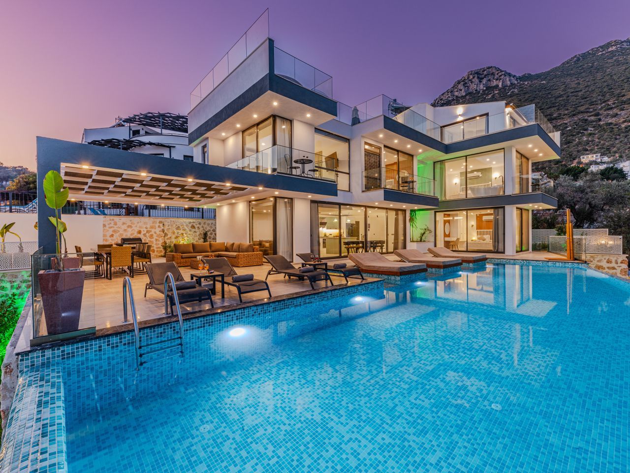 The villa lit at dusk beside its pool